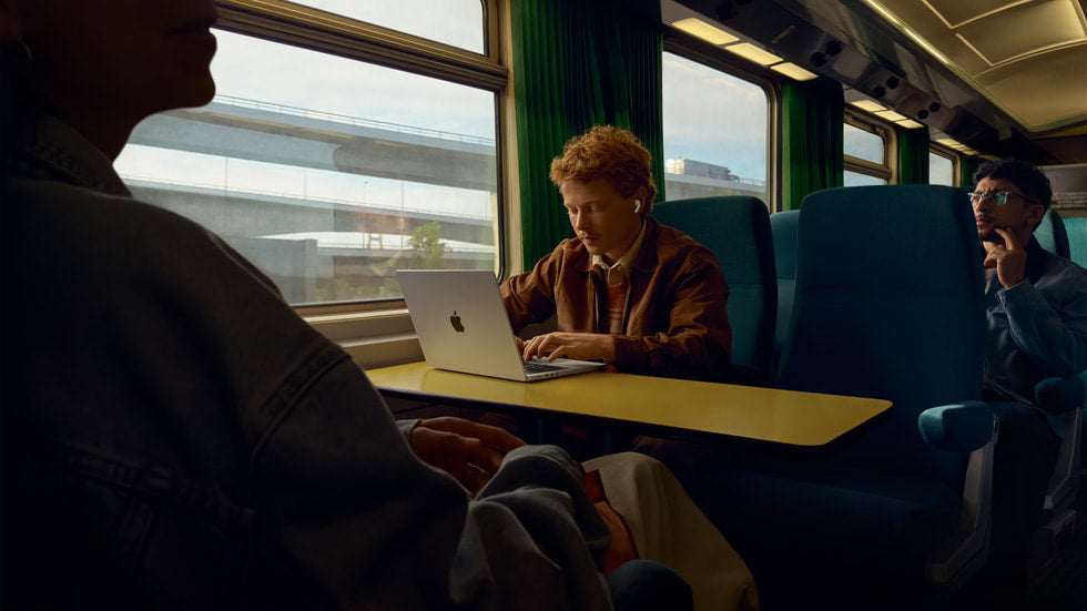 Una hombre usando sus AirPods con una Macbook en un tren.